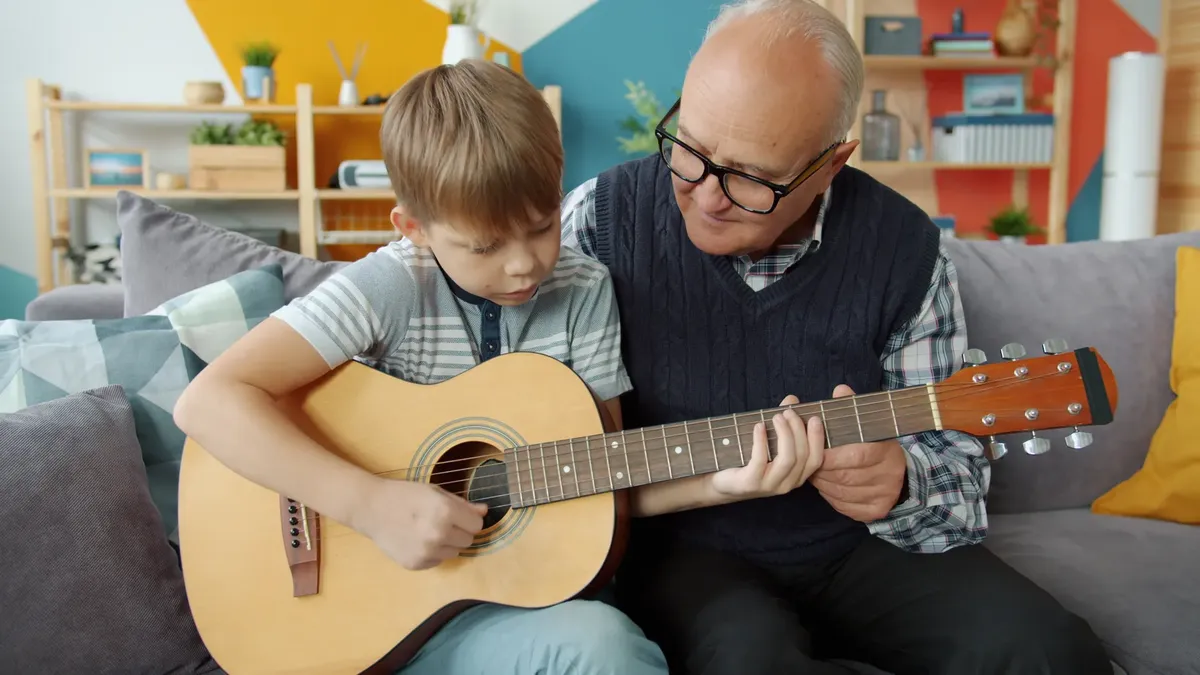 A grandfather and grandson bond over music, playing guitar together in a cozy living room.